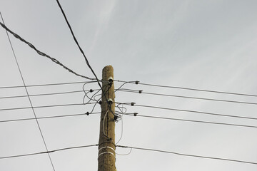 An old electric wooden pole with electricity cables hanging on it