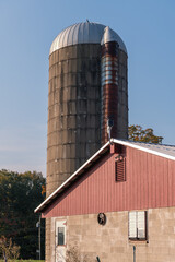 A photograph of an old barn and silo on a farm against the sky