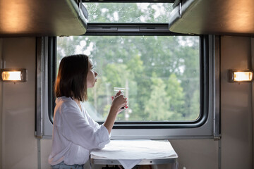 A young beautiful woman in a white shirt is sitting in a train compartment with a Cup of tea and...