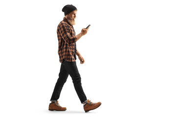 Full length profile shot of a young man in checkered shirt and jeans walking and using a mobile...
