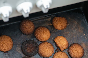 Burnt cookies. Burnt, burnt oatmeal cookies lie on a black baking sheet. Vertical photo