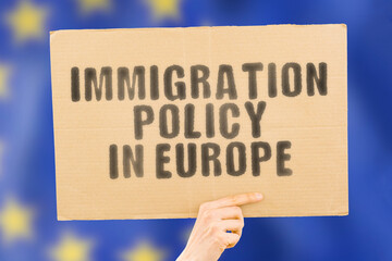 The phrase " Immigration Policy in Europe " on a banner in men's hand with blurred European Union flag on the background. Immigrants. Rules. Legislation. Law. Legal