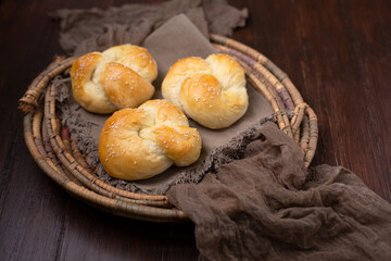 Three Homemade Kaiser Rolls Topped with Sesame Seeds in an Old Woven Bread Basket on a Wood Table