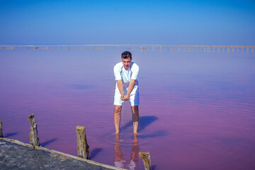Brunet man relaxing on pink salty Sivash Lake near Azov Sea, colored by microalgae Dunaliella salina, enriching water of the lake by beta-carotene
