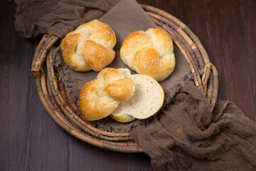 Three Homemade Kaiser Rolls Topped with Sesame Seeds in an Old Woven Bread Basket on a Wood Table