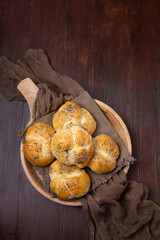 Top View of Homemade Kaiser Rolls Topped with Poppy Seeds in a Round Wooden Bowl on a Wooden Table
