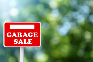 Sign with phrase GARAGE SALE on blurred green background, bokeh effect
