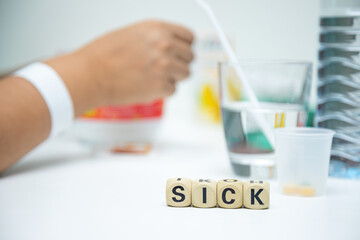 Sick wording on wooden block on table with medicine and water glass for patient