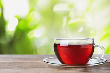 Glass cup of fresh hot tea on wooden table against blurred green background. Space for text