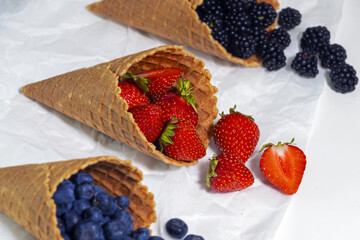 Waffle cone with delicious berries on white background