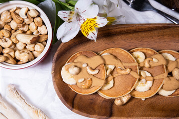 Pancakes with mix of nuts and peanut butter on white background with flowers. Trendy food.