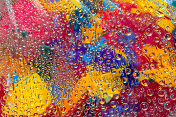 Water droplets flow down on the multicolored glass mosaic. Close-up.