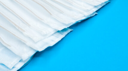 Many antiviral protective medical face masks with earloops are set against a blue background....