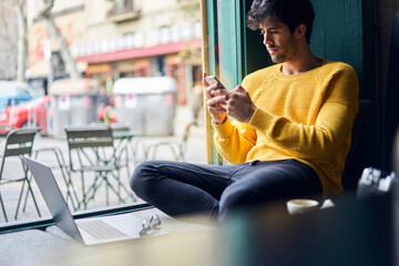 Crop young man browsing smartphone in modern workspace