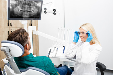 Woman dentist prepares to work with the male patient. Dentist adjusting protective glasses while...