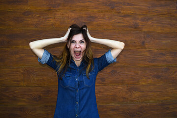 Young brunette woman opened her mouth holding her head on a brown background