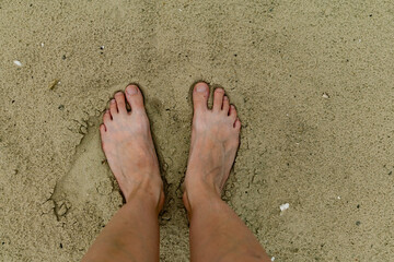 Feet naked barefoot without shoes burrow in the sand on a sandy beach, white skin and toes make...