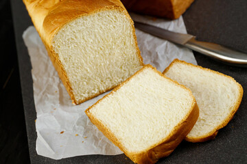 Sliced white bread with knife on a waxed sheet dark background. Bakery copy space.
