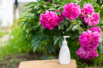 white cosmetic bottle for soap or shampoo on wooden shelf with peonies background. For montage of your product.