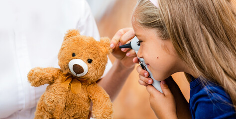 little girl looking through the otoscope on the toy's ear. Hearing check-up, funny child