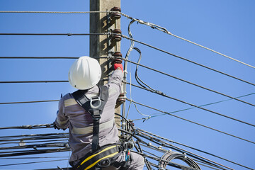 A workers climbs an electric pole to fix a broken wire wearing full safety harness and PPE for safety concept