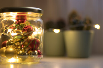 Christmas decorations inside a glass jar and warm lights in the background.