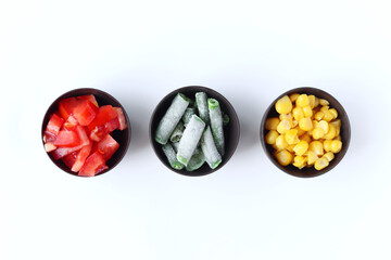 Variety of cut vegetables in bowls isolated on white background. Tomatoes, green beans and corn.