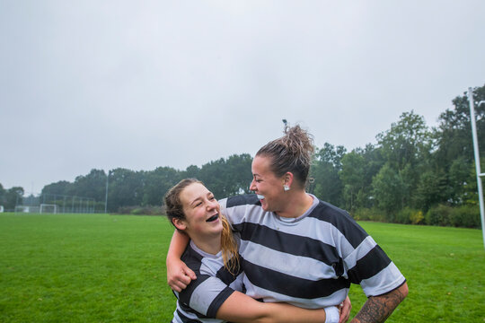Two female rugby teammates hugging and looking at eachother.