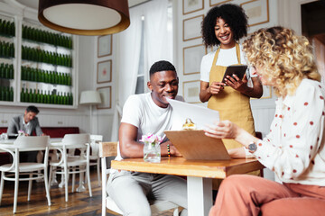 Cheerful waitress taking order from diverse couple