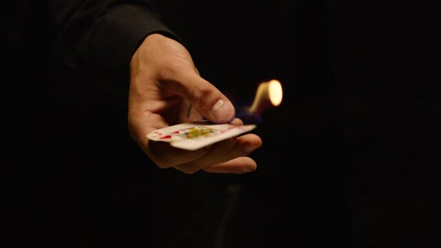 Close-up of a Magician Hand Performing Card Trick . Burning card on black Background with smoke . Card Mechanic rotating flaming card in hand . Shot on ARRI Alexa cinema camera in Slow Motion