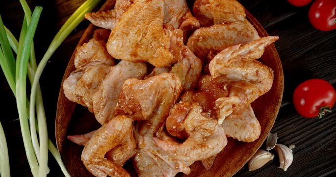 Marinated raw chicken wings with tomatoes and onions rotate. 