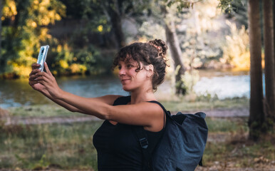 Hiker woman with a backpack taking a selfie with the smartphone during a walk in the forest. Adventurous woman, travel blogger