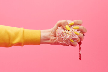 Woman with yellow nails squeezes a jammy iced pink doughnut in her hand