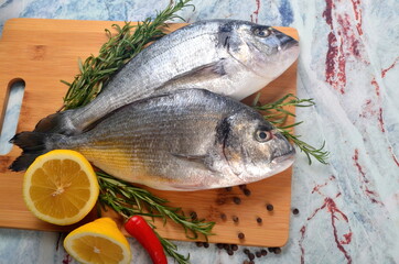Two Fresh Dorado fish with lemon, onion and rosemary on light marble background, top view