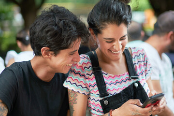 Cheerful Hispanic hipster couple using smartphone together on street