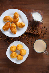 A transparent mug with coffee with cream and a jug of cream and croissants and cookies on the table among the scattered coffee beans.
