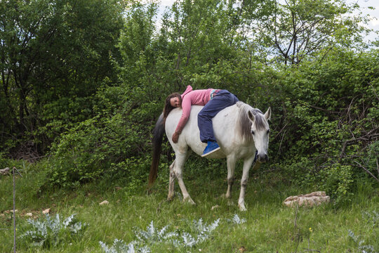 Woman lying backwards on white horse in nature