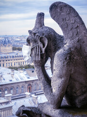 COVID-19 coronavirus in France, surgical mask on gargoyle of Notre Dame in Paris.