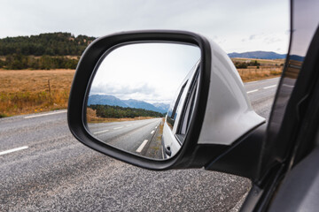 Rear view mirror of an adventure camper van showing a beautiful road. The road goes towards the mountains. Stop for a road trip.