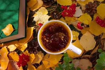 A cup of fresh hot tea is among the autumn leaves, cones, berries, rose hips. Spectacular splash in the cup. Concept for natural drinks, hiking, camping, autumn season. View from above.