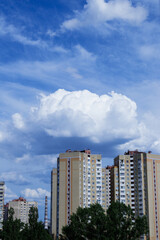 Cloudy blue sky and huge cumulus clouds above the top of the buildings.