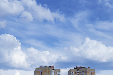Cloudy blue sky and  huge cumulus clouds above the top of the buildings.