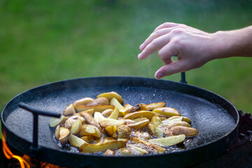 the cook salts the potatoes which are fried on an open fire in oil, copy space. out of doors