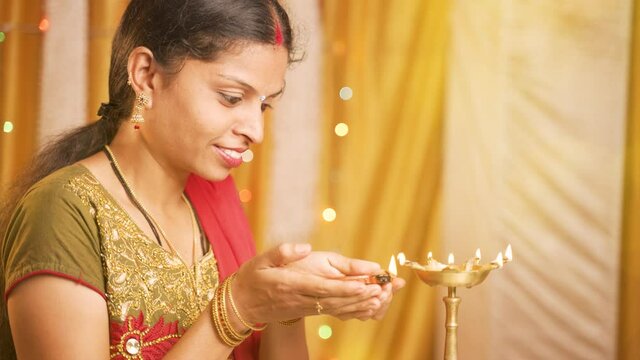 Happy smiling Indian woman lighting lantern or Diya Lamp during festival ceremony at home - concept of diwali traditional festival and ritual celebrations