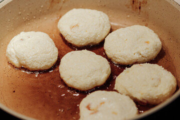 Cooking process of delicious fried syrniki close-up in the pan. Traditional in Ukraine, Belarus and Russia quark pancakes. Selective focus.