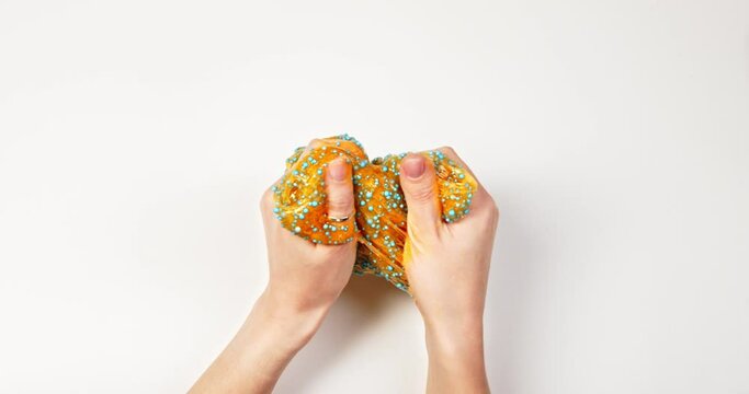 Playing with textured slime with bubbles, stretching the gooey substance for fun and stress relief. Close up and top view of female hand holding orange shining slime, squeezing it.