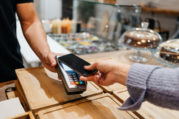 Detail of a client hands paying with the smartphone at a restaurant