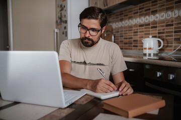 Concentrated millennial hipster guy wearing glasses, listening to favorite music while planning workday.