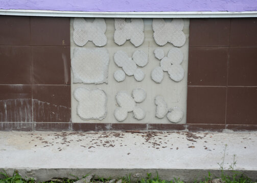 A Close-up On The House Foundation, External Wall With Tiles Fallen Off Because Of Uneven Wall, Thick Layer Of Adhesive Or Water Getting Behind The Tiles And Deteriorating The Adhesive.