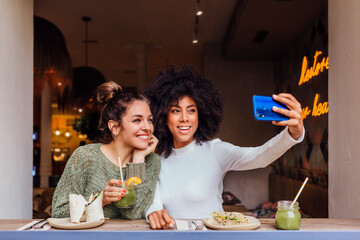 Cheerful multiethnic women taking selfie in cafe